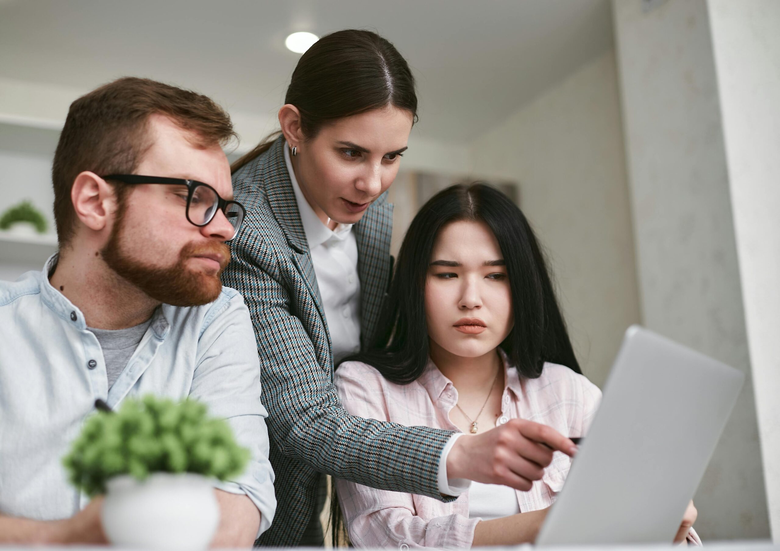 Three colleagues engaged in a focused teamwork session using a laptop in a modern office environment.